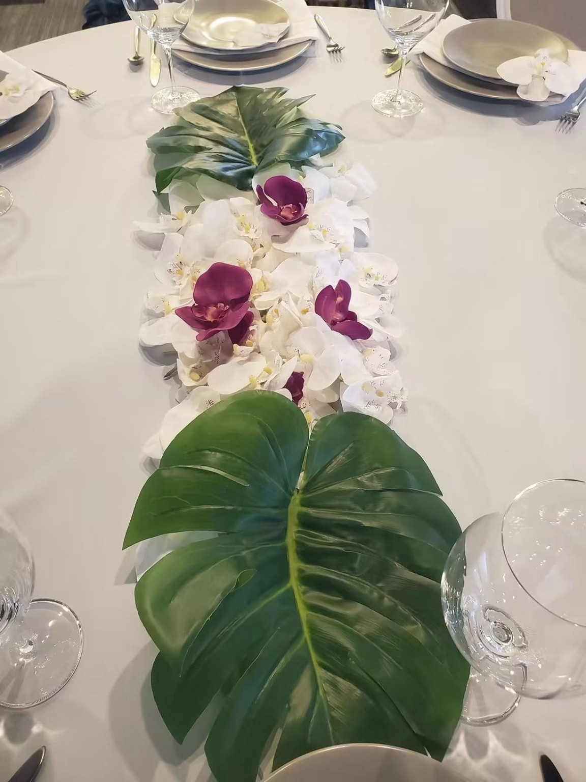 Green leaves and orchids arranged down a table